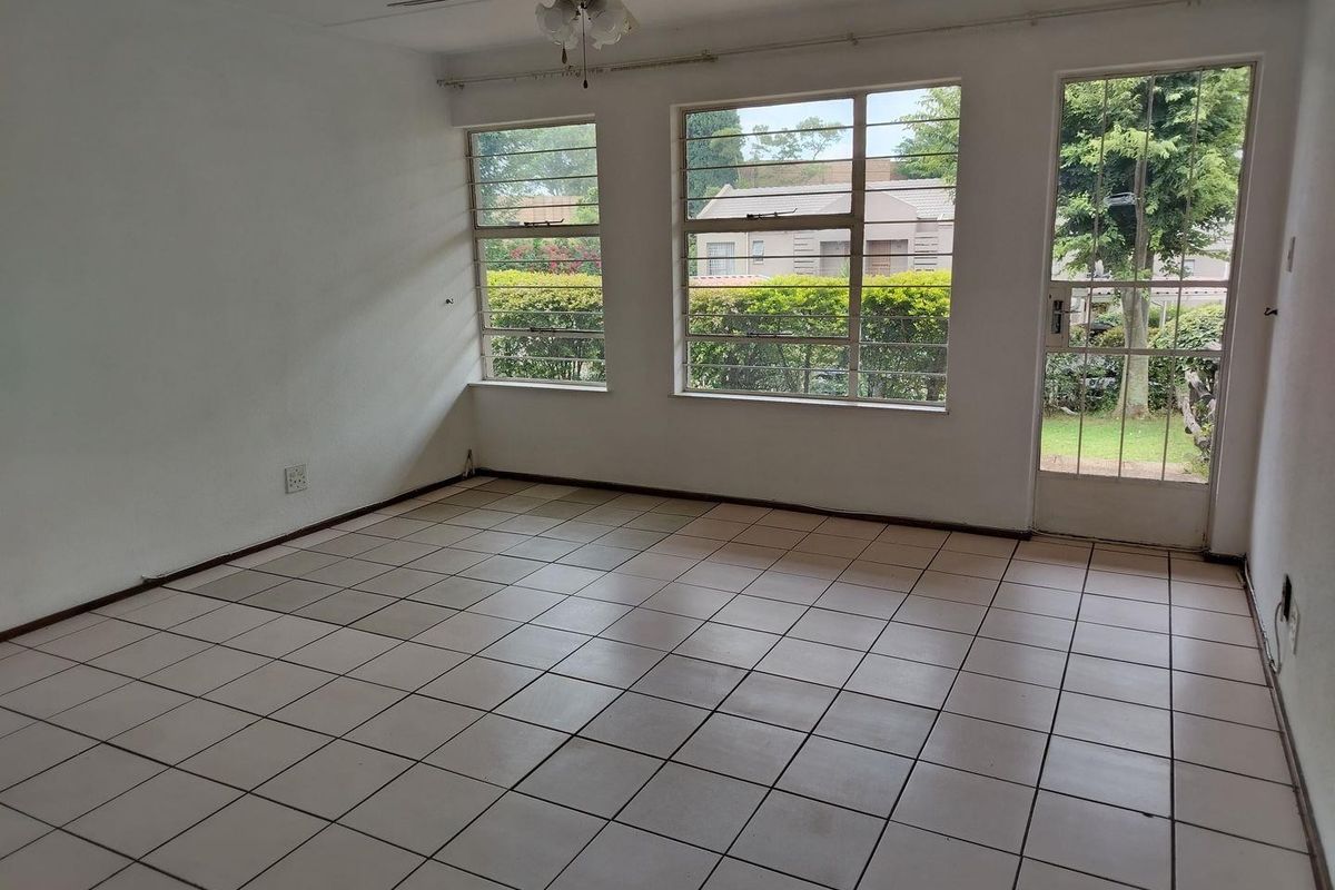 An empty living room featuring tiled flooring, a ceiling fan, and large windows providing natural light and access to the exterior.