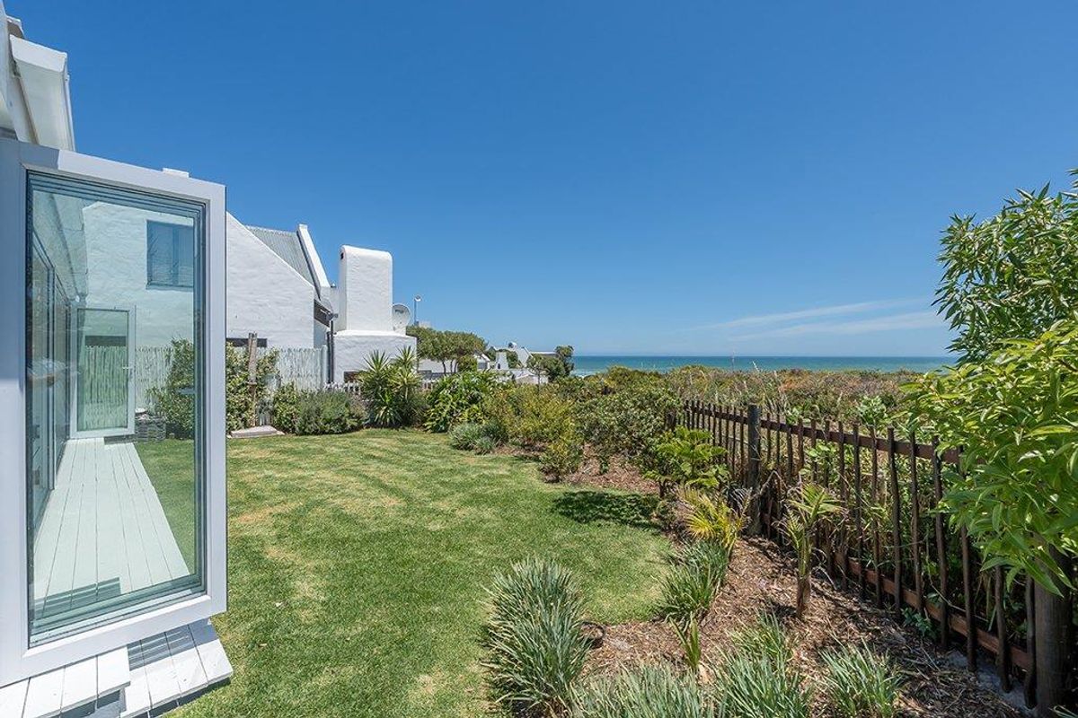 A well-maintained rear garden featuring a manicured lawn, established coastal landscaping, and a clear view of the ocean.