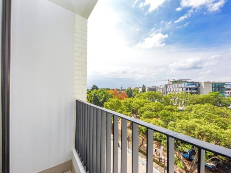 A clean, modern balcony featuring a sleek metal balustrade and offering elevated views over the surrounding trees and urban landscape.