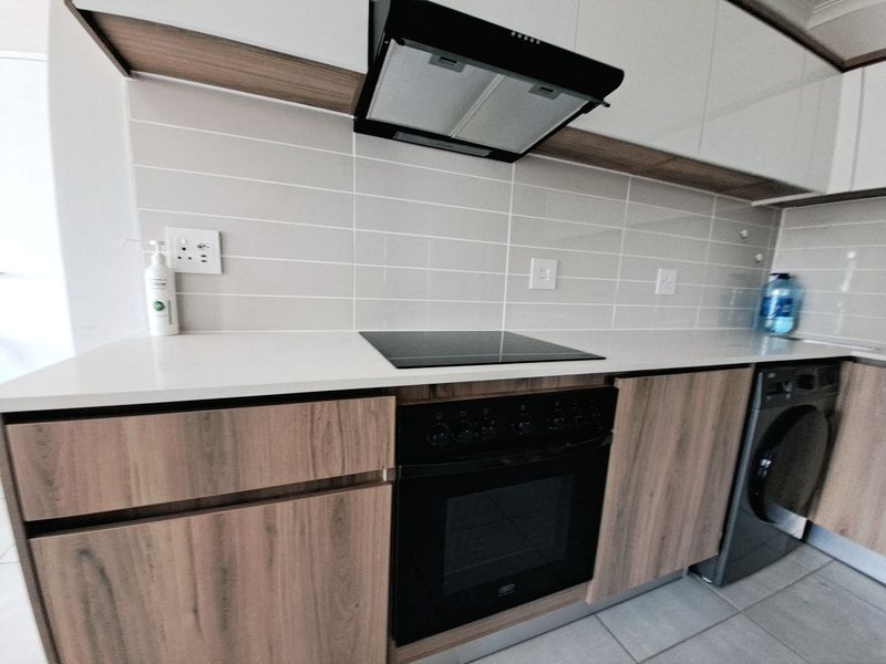 Modern kitchen featuring sleek laminate cabinetry, quartz countertops, a built-in oven with electric hob, extractor fan, and subway tile backsplash.
