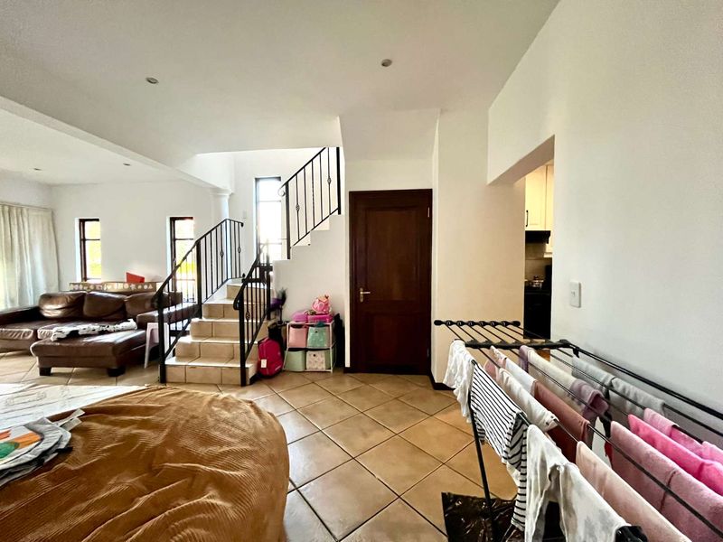 Open plan living area featuring tiled flooring, a staircase with wrought iron railings, and recessed lighting, leading towards a kitchen area.