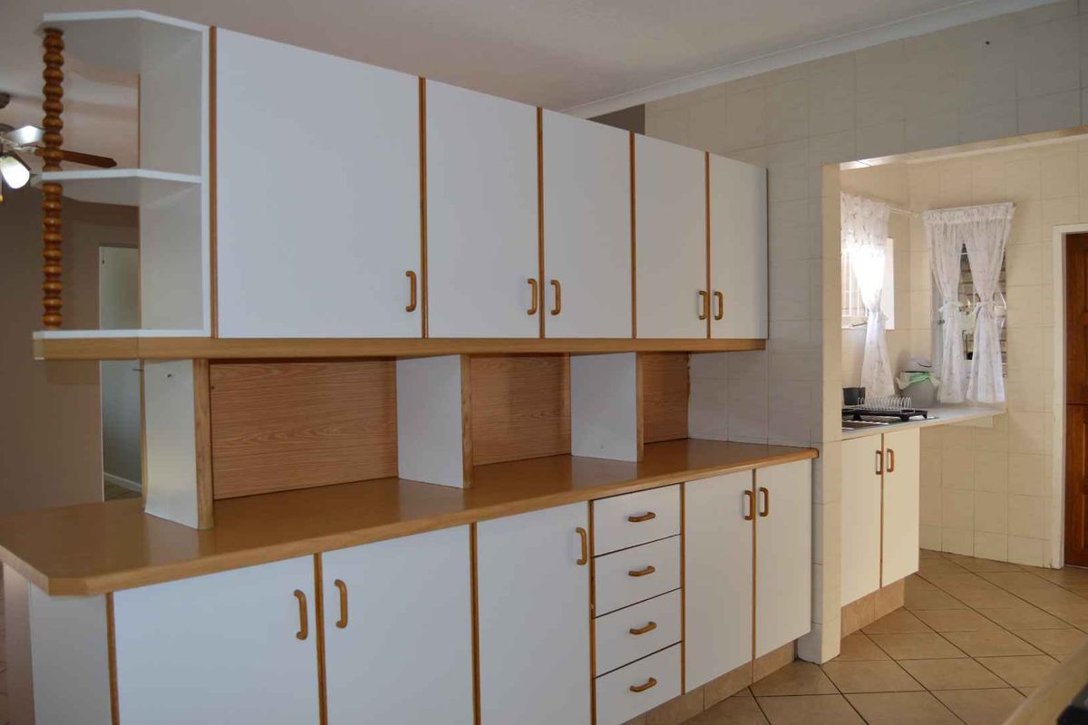 A functional kitchen featuring white built-in cabinetry with wood trim, laminate countertops, and tiled flooring, offering a clean and practical workspace.