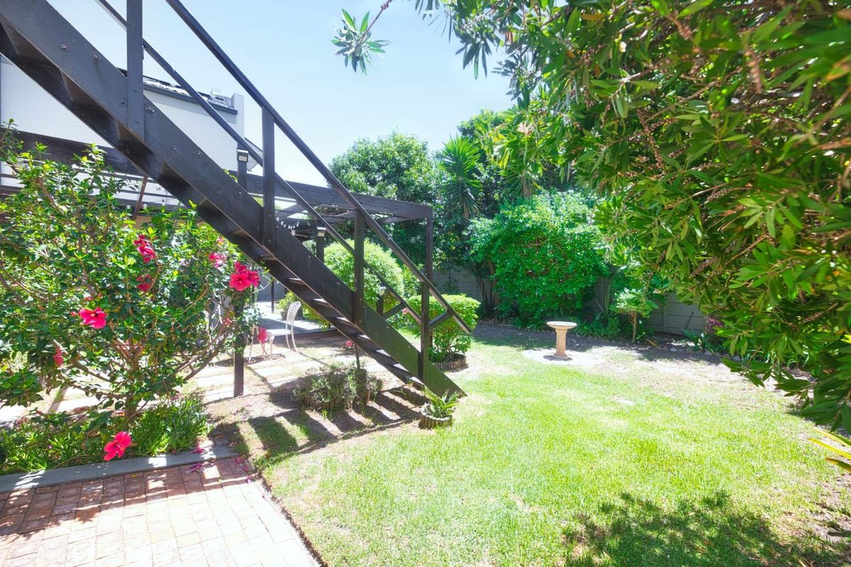 A private rear garden featuring a lawn, established greenery, and an external staircase leading to an upper level.