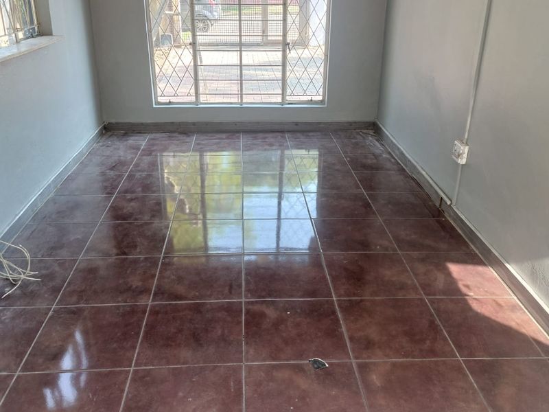An empty living room featuring dark tiled flooring, security bars on the windows, and a security gate leading to the exterior.
