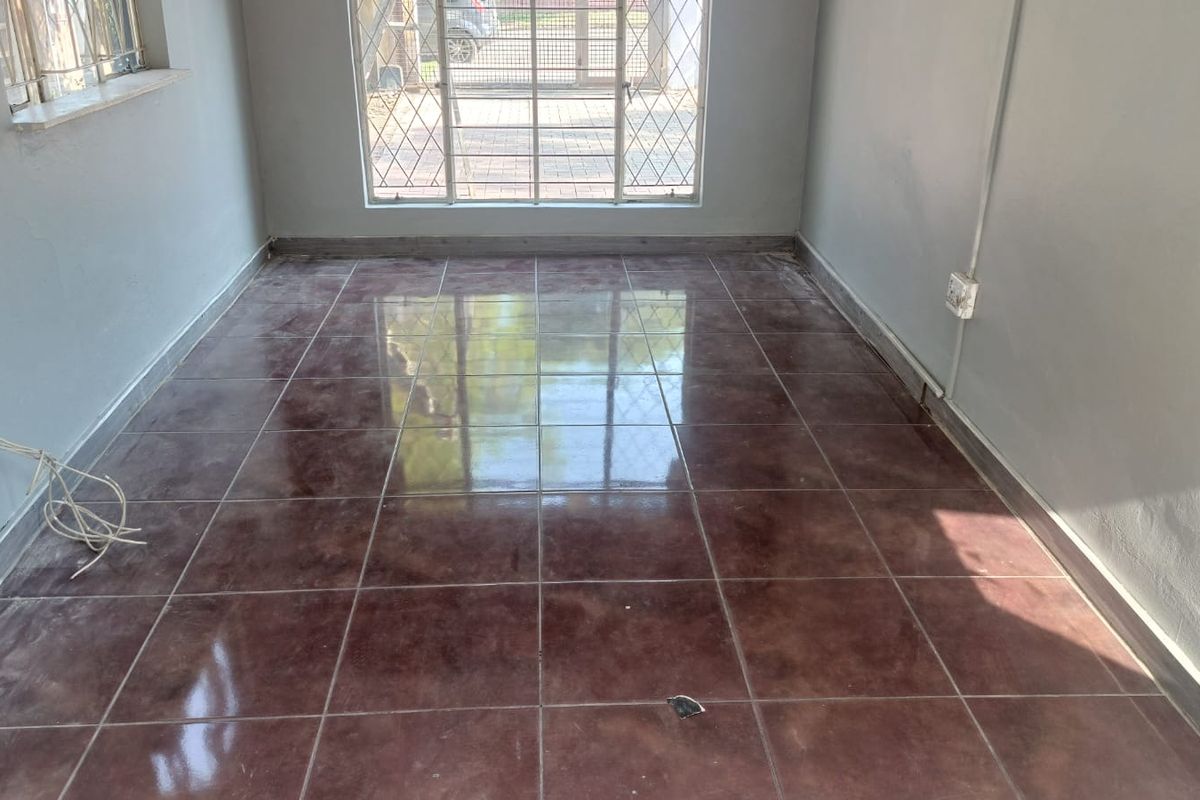 An empty living room featuring dark tiled flooring, security bars on the windows, and a security gate leading to the exterior.