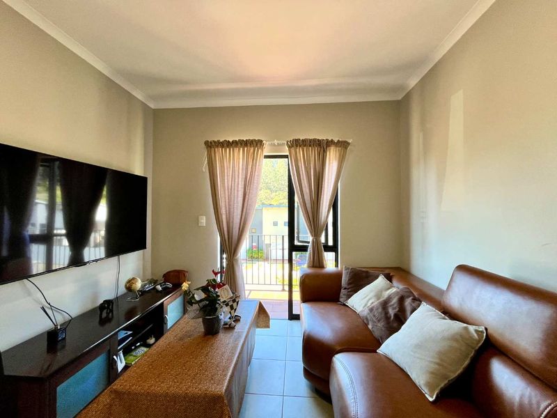 A comfortable living room featuring tiled flooring, coved ceilings, and a sliding glass door providing direct access to an outdoor balcony.