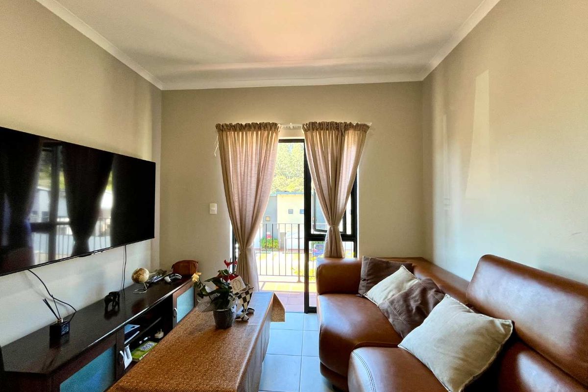 A comfortable living room featuring tiled flooring, coved ceilings, and a sliding glass door providing direct access to an outdoor balcony.
