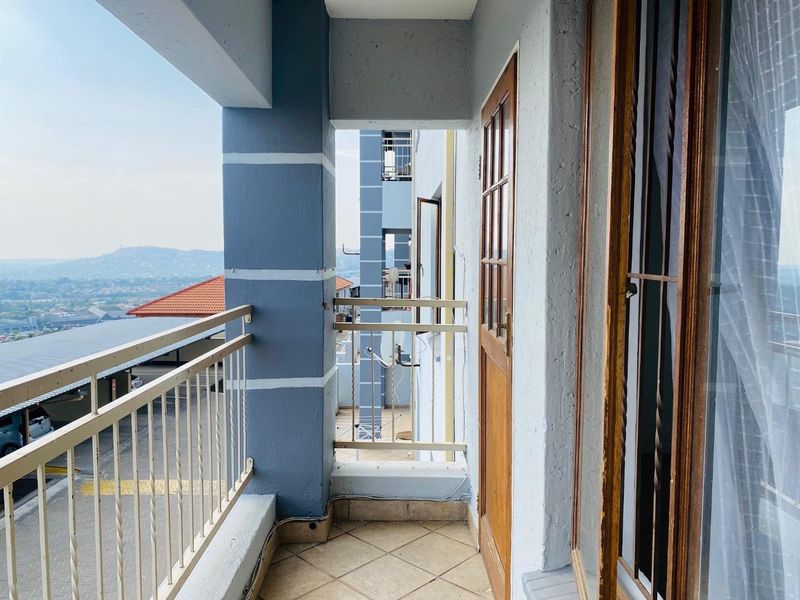 A covered balcony featuring tiled flooring, a metal balustrade, and timber-framed access points, offering elevated views of the surrounding area.