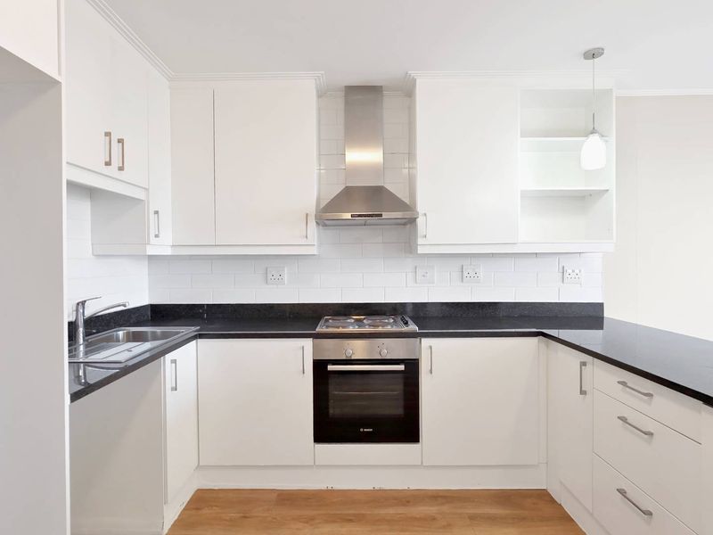 A modern, well-maintained kitchen featuring white cabinetry, black granite countertops, a subway tile backsplash, and integrated stainless steel appliances.