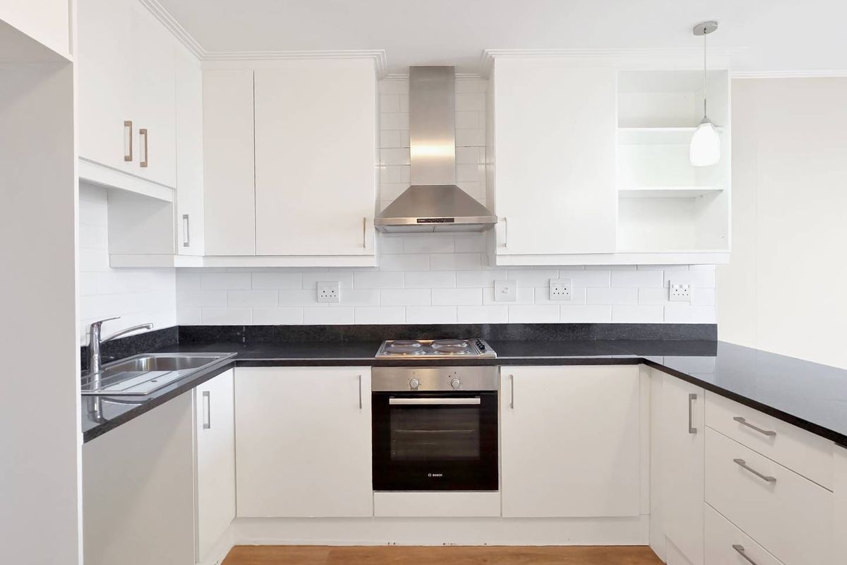 A modern, well-maintained kitchen featuring white cabinetry, black granite countertops, a subway tile backsplash, and integrated stainless steel appliances.