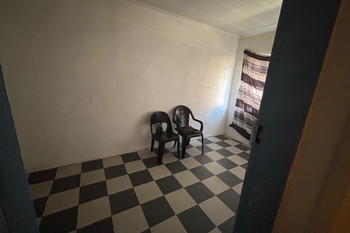 A simple, vacant bedroom featuring checkered floor tiles and plain white walls, offering a blank canvas for potential renovation or interior design updates.