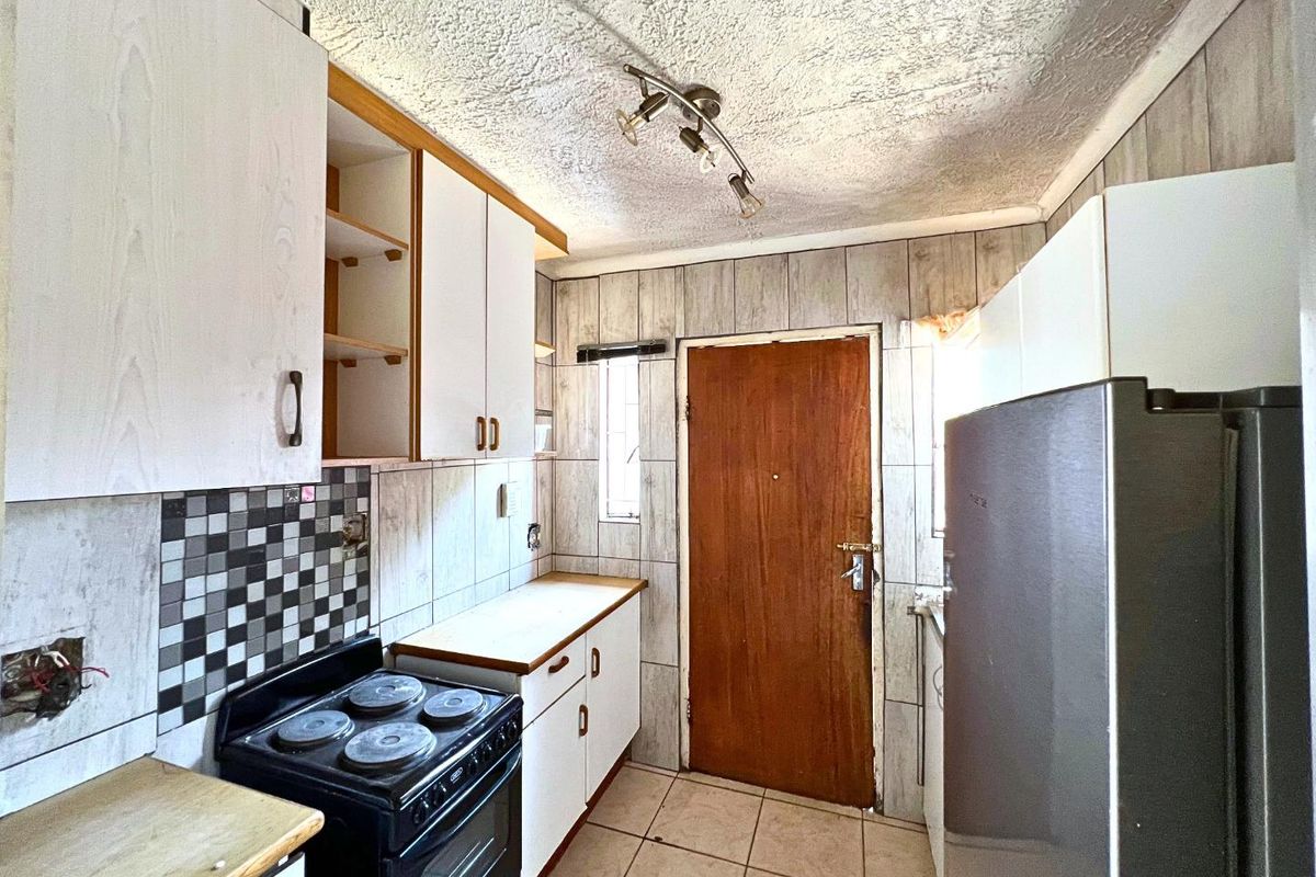 A dated kitchen featuring built-in cabinetry, tiled backsplash, and tiled flooring, requiring cosmetic updates to modernize the space.