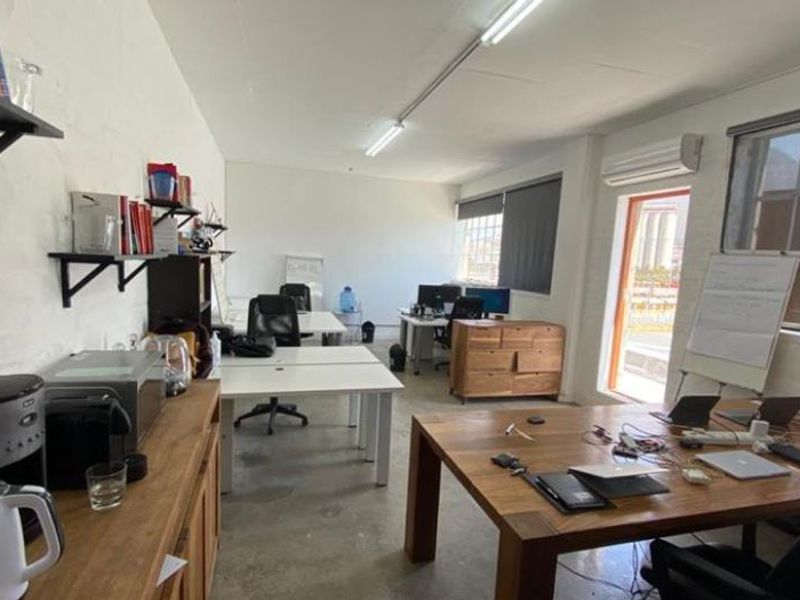 A functional office space featuring concrete flooring, large windows for natural light, and a wall-mounted air conditioning unit.
