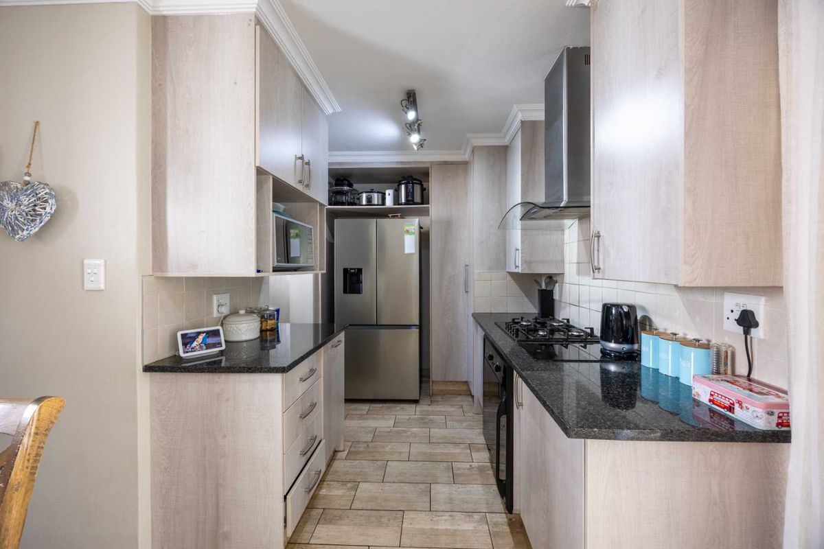 A well-maintained galley-style kitchen featuring light wood-finish cabinetry, dark granite countertops, a gas hob, and a stainless steel extractor fan.