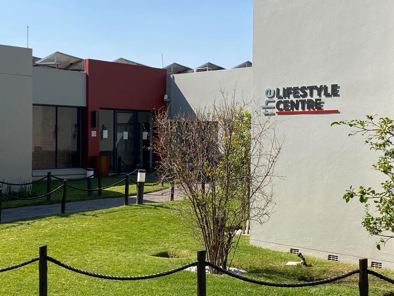 Exterior view of the apartment complex lifestyle centre featuring modern facade, signage, and landscaped garden area with paved pathways.