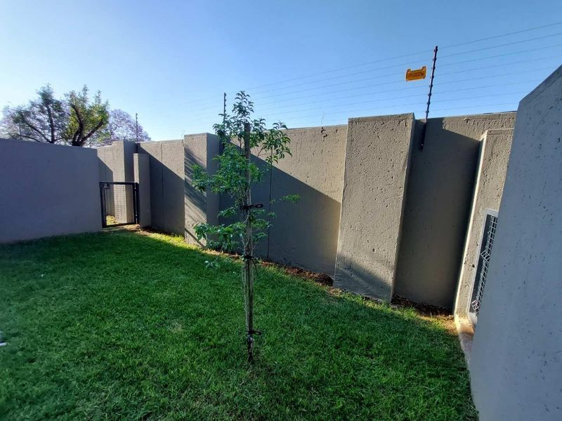 A private rear garden area featuring a well-maintained lawn, enclosed by high perimeter walls with integrated electric security fencing.