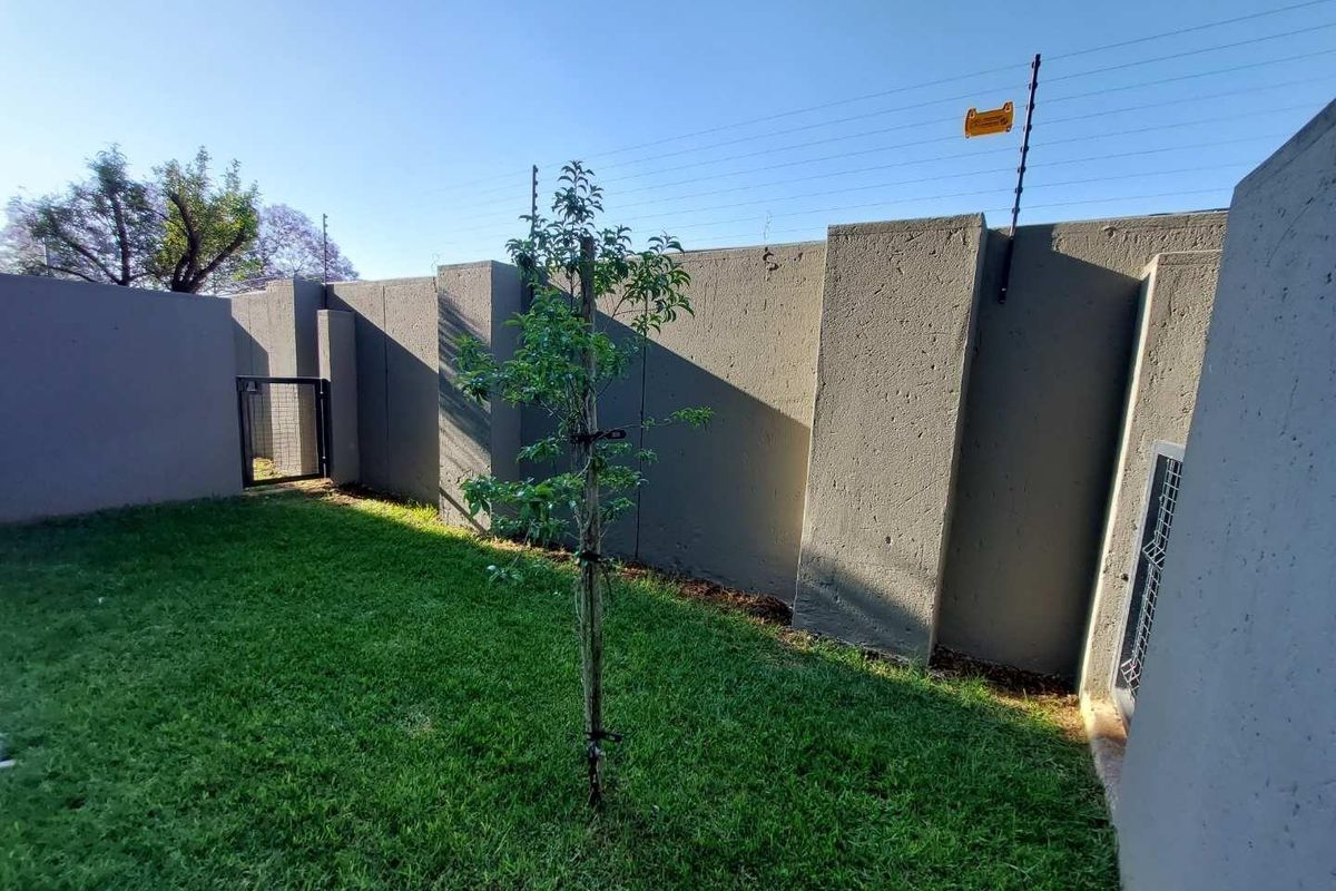 A private rear garden area featuring a well-maintained lawn, enclosed by high perimeter walls with integrated electric security fencing.