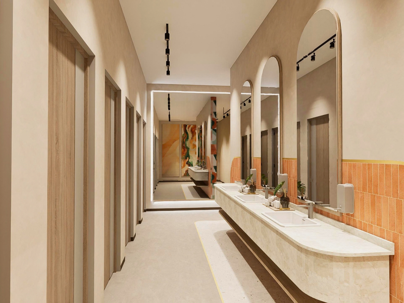 Modern, high-end office bathroom featuring a long integrated vanity with dual basins, arched mirrors, and stylish terracotta-toned tiled accents.