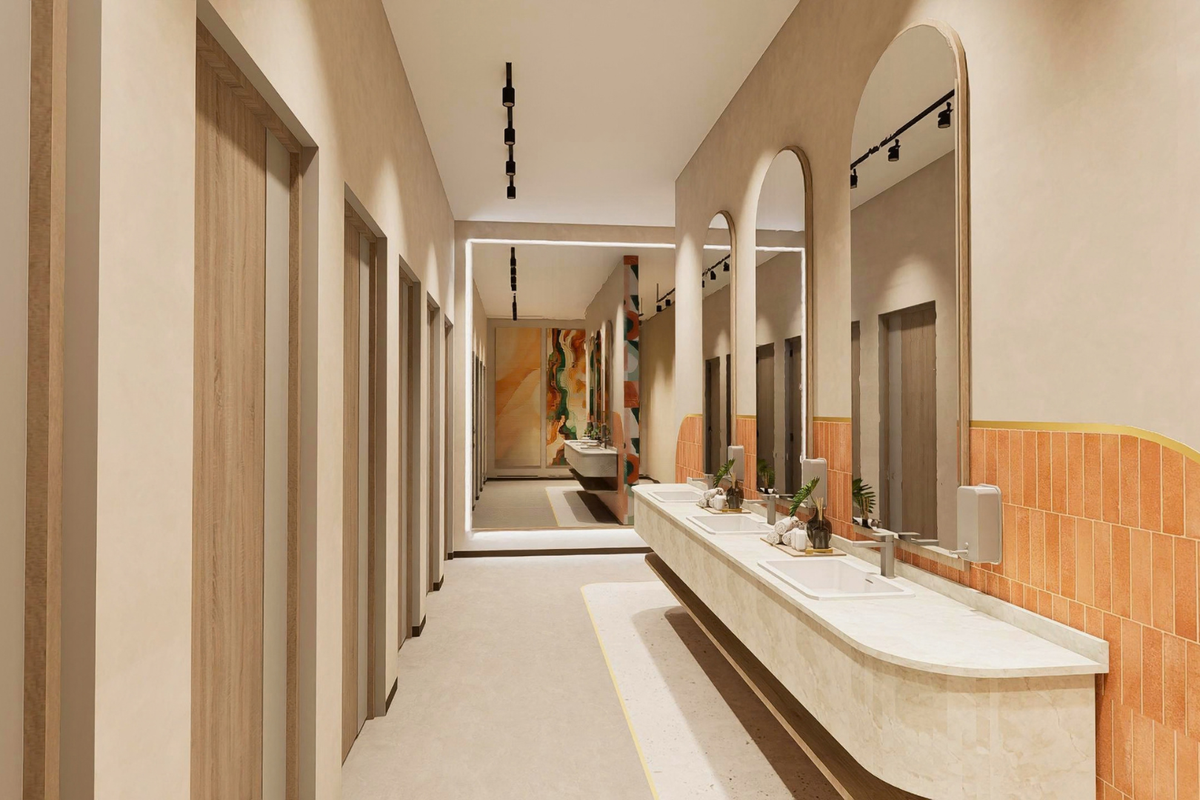 Modern, high-end office bathroom featuring a long integrated vanity with dual basins, arched mirrors, and stylish terracotta-toned tiled accents.