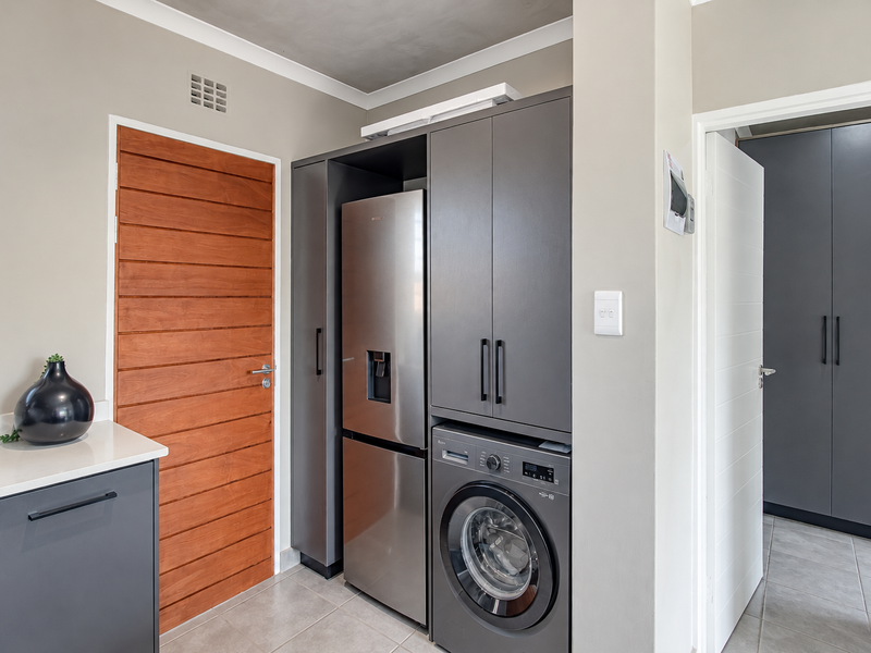 A modern, well-appointed laundry area featuring sleek grey cabinetry, integrated washing machine, stone countertops, and tiled flooring.