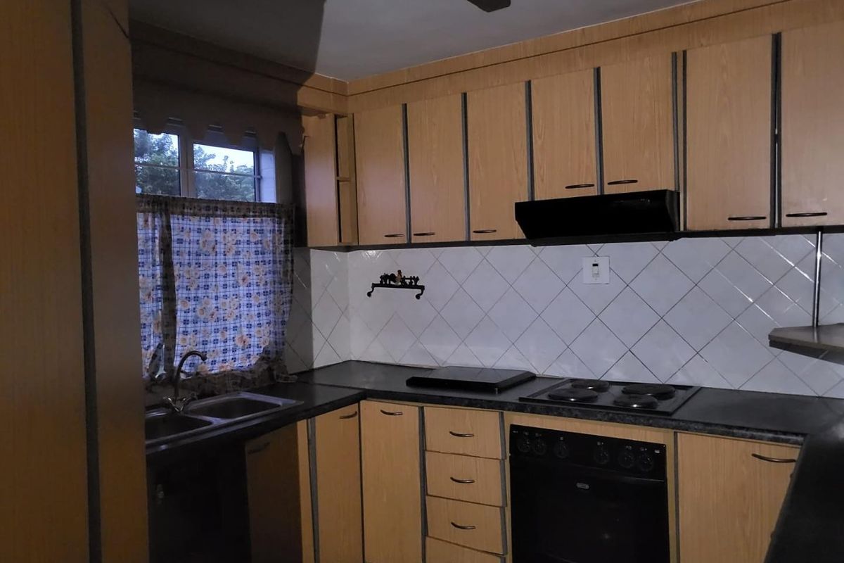 A functional kitchen featuring wood-look laminate cabinetry, built-in oven, electric hob, extractor fan, and a double bowl sink with tiled backsplash.