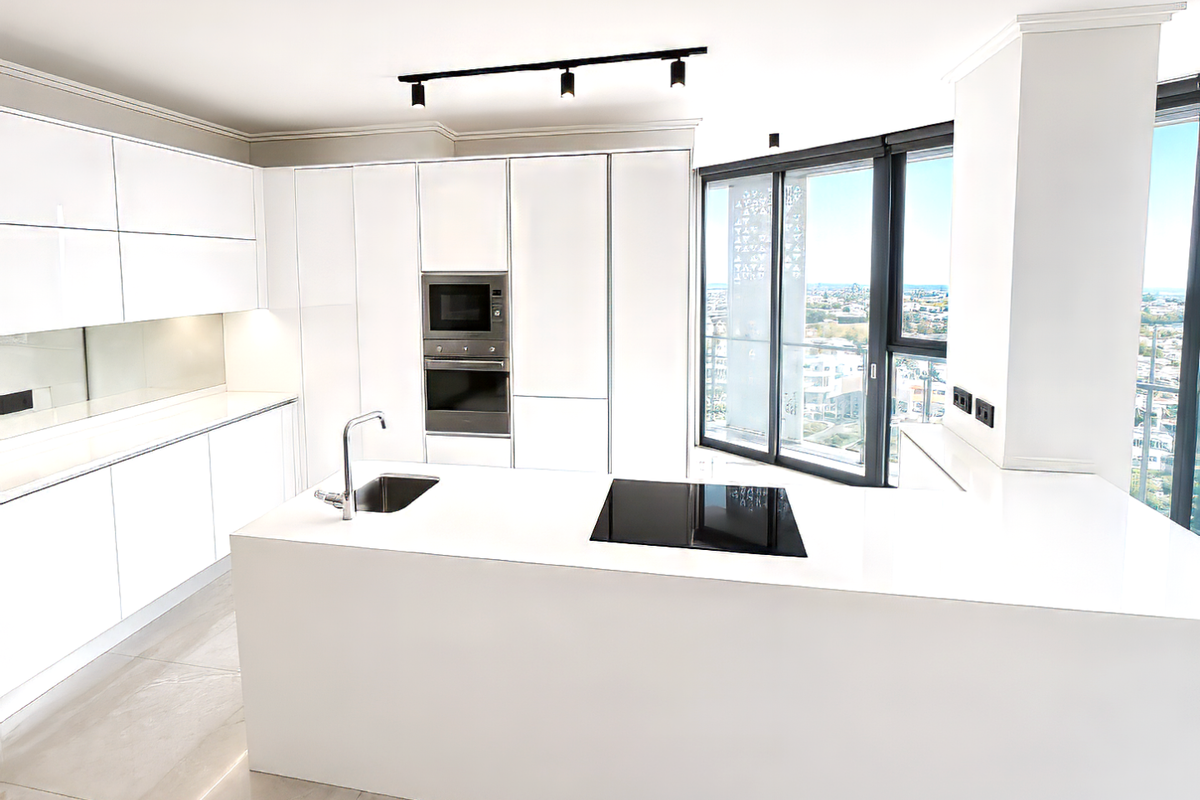 Modern open-plan kitchen featuring sleek white cabinetry, integrated oven and microwave, induction hob, and a central island with a sink, overlooking city views.
