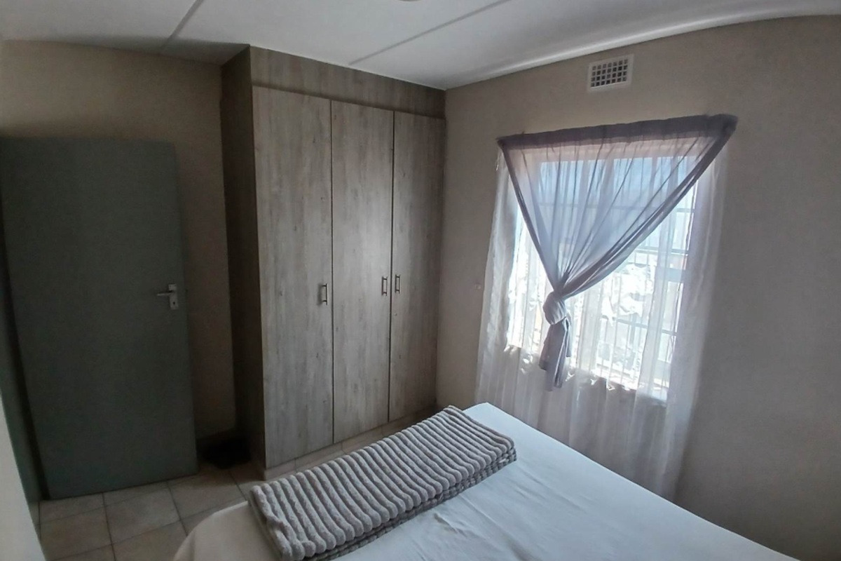 A bedroom featuring built-in wooden cupboards, tiled flooring, and a window with natural light.