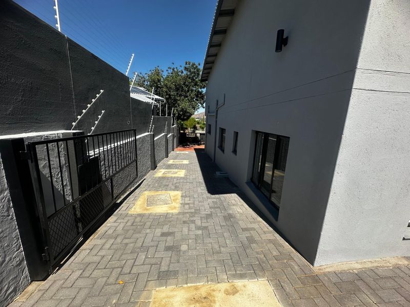 A clean, paved side passage featuring secure boundary walls with electric fencing and modern exterior wall lighting.