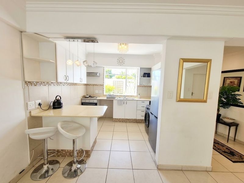 A functional kitchen featuring built-in cabinetry, a breakfast bar, tiled backsplash, and integrated appliances, with a clean layout and tiled flooring throughout.
