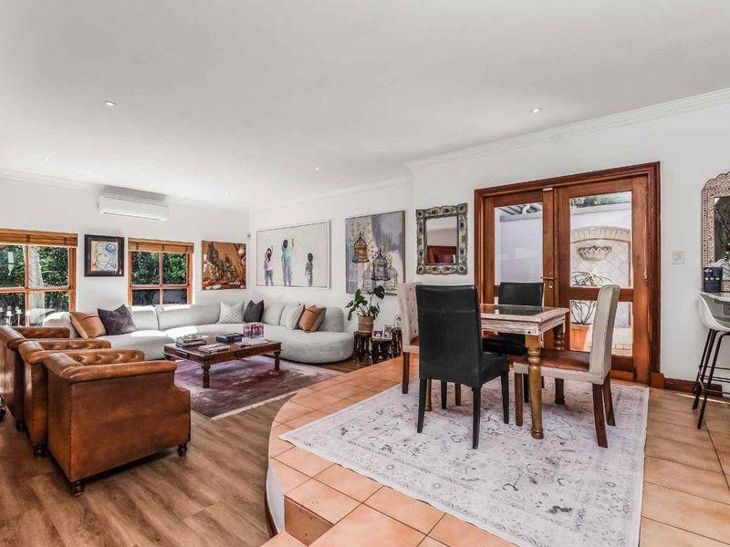 Spacious open-plan living and dining area featuring timber-look flooring, a raised tiled dining section, and direct access to the outdoor space through glass doors.