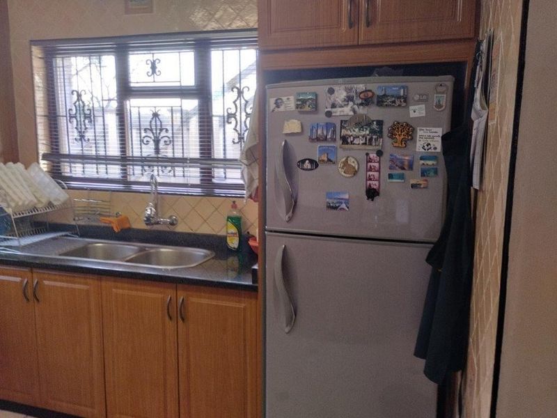 A functional kitchen area featuring laminate cabinetry, granite countertops, a double bowl sink, and a tiled backsplash with window security bars.