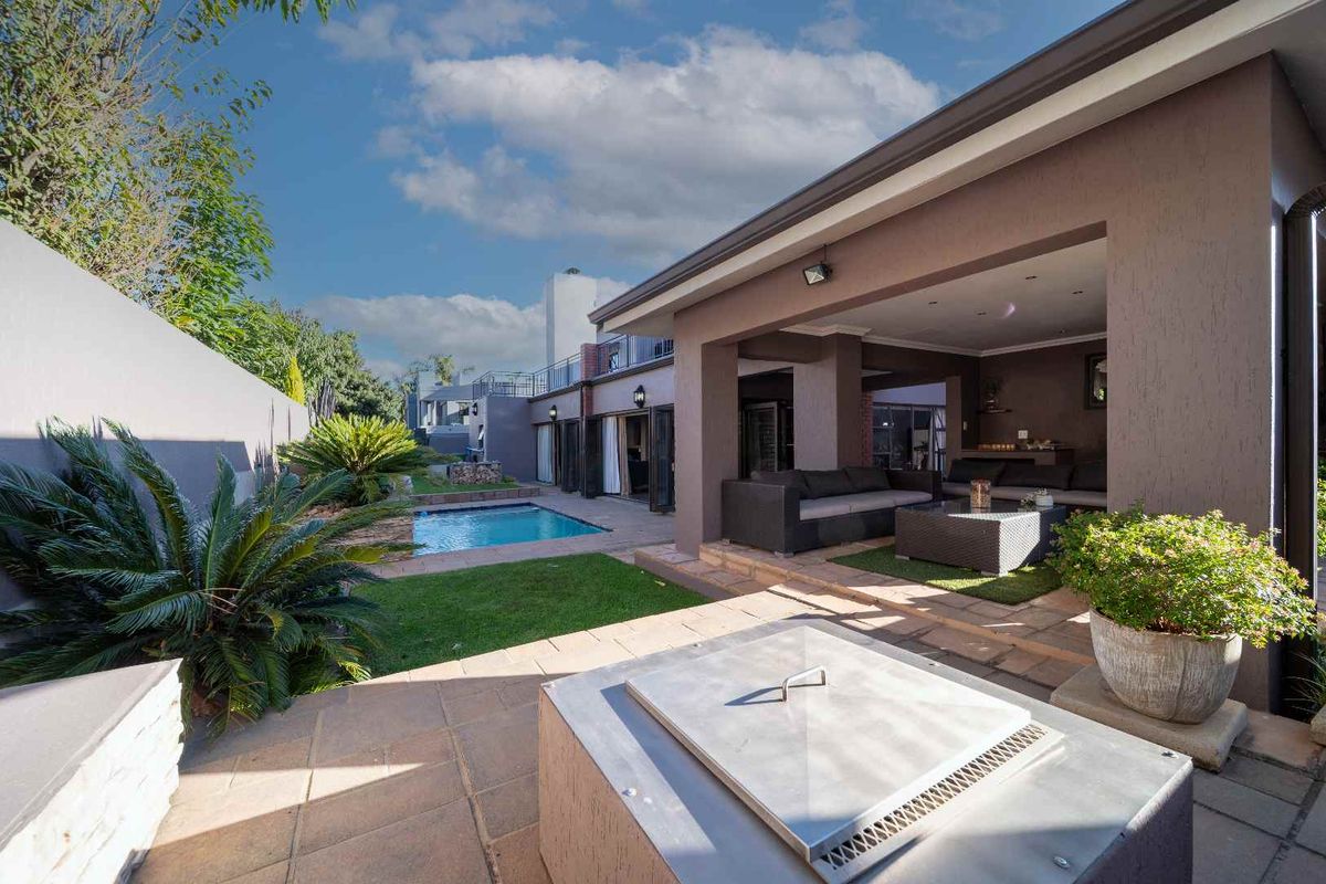 A spacious covered patio overlooking a private swimming pool and landscaped garden, featuring a built-in fire pit and seamless indoor-outdoor flow.