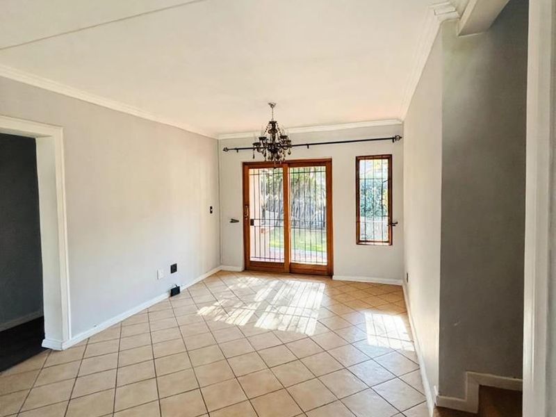 An empty living room featuring tiled flooring, crown molding, and a sliding glass door with a security gate leading to the exterior.
