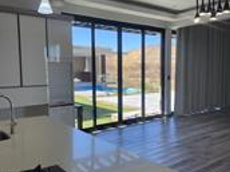 Modern open-plan kitchen and living area featuring stone countertops, a gas hob, and large sliding glass doors opening to a pool and garden.