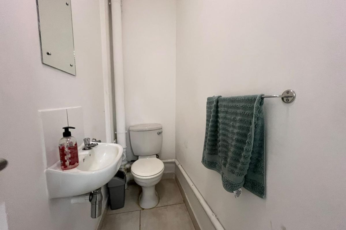 A compact guest bathroom featuring a wall-mounted basin, toilet, and exposed plumbing, requiring cosmetic updates to improve its overall aesthetic.