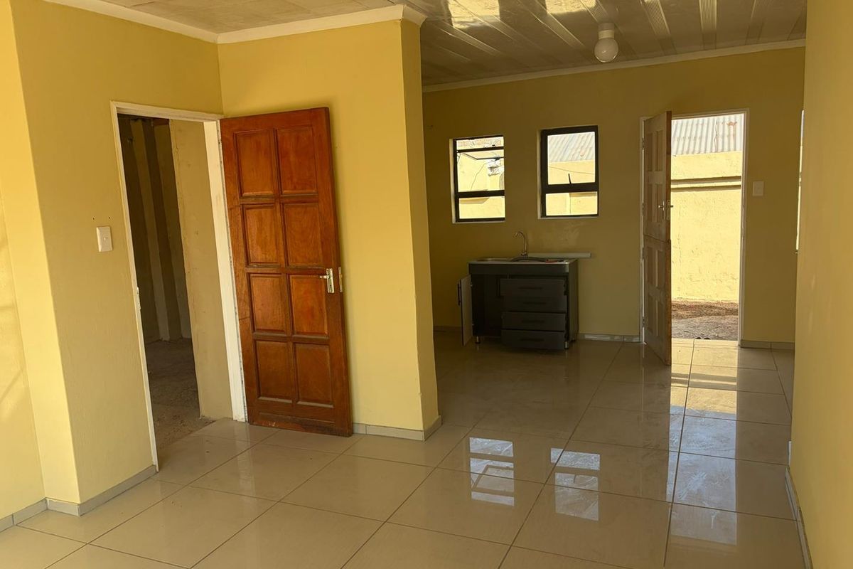An open-plan living area featuring tiled flooring, a basic kitchen sink unit, and direct access to the exterior.