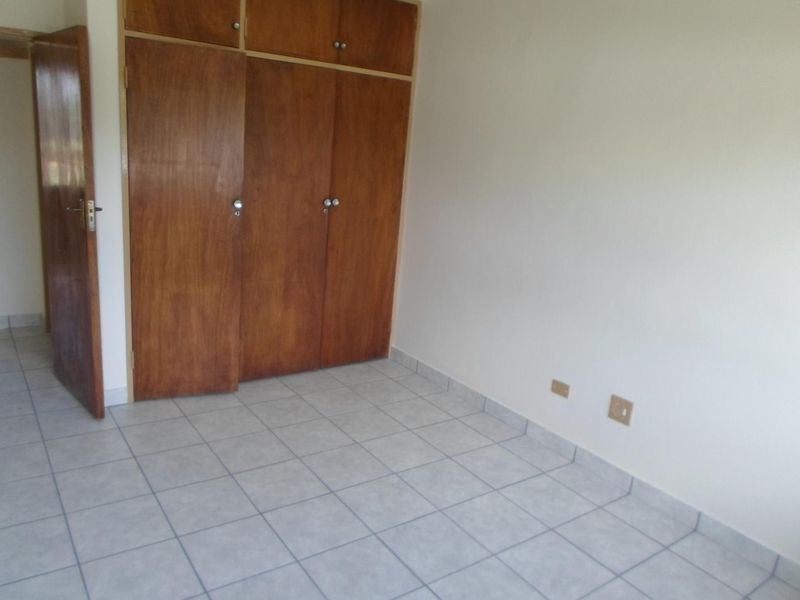 An empty bedroom featuring tiled flooring and built-in wooden cupboards, providing a clean and functional space ready for personalization.