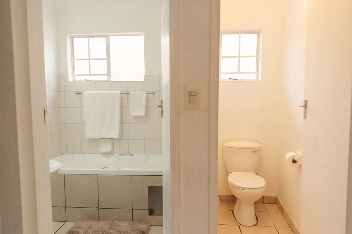 A functional bathroom featuring a bathtub and a separate toilet area with tiled finishes and natural light.