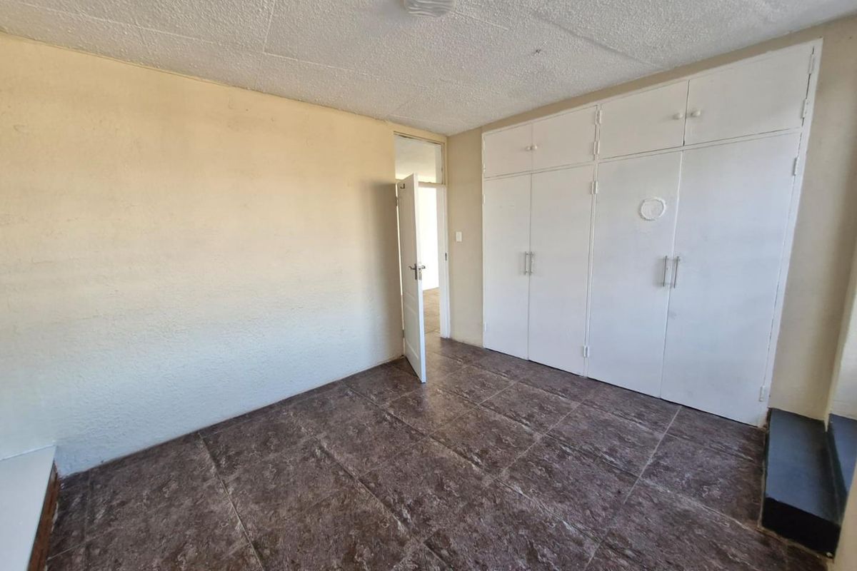 A vacant bedroom featuring dark tiled flooring and extensive white built-in cupboards, offering a blank canvas for renovation.