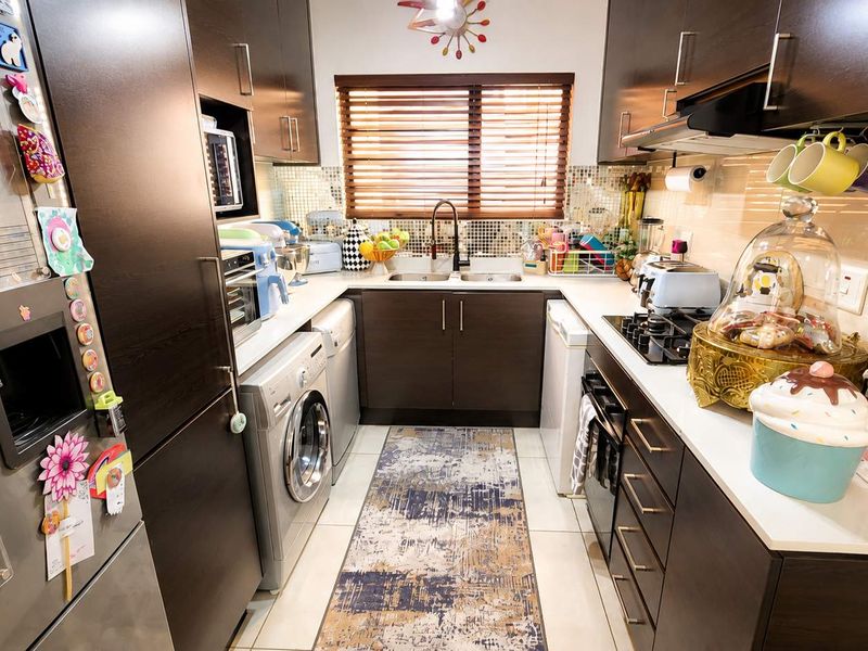 A compact, functional kitchen featuring dark wood cabinetry, mosaic tile backsplash, integrated appliances, and a gas hob with an extractor fan.