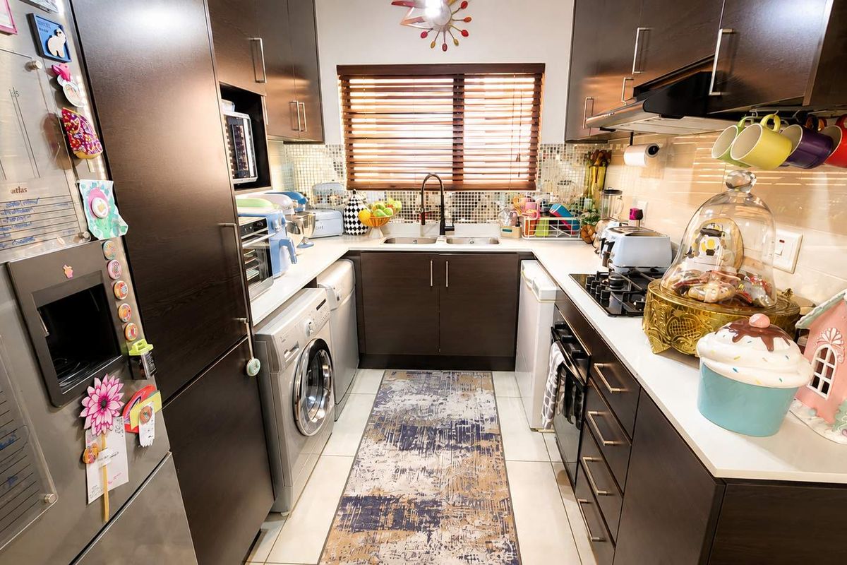 A compact, functional kitchen featuring dark wood cabinetry, mosaic tile backsplash, integrated appliances, and a gas hob with an extractor fan.