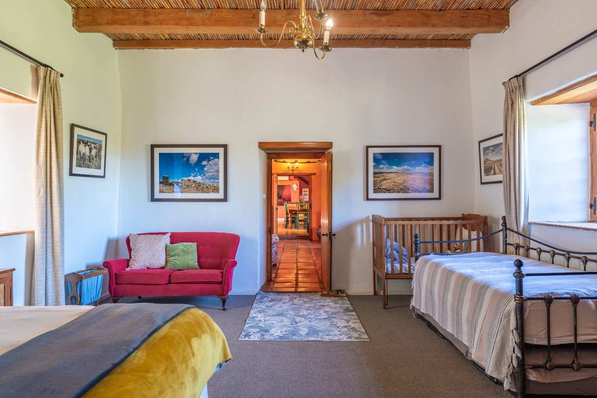 Spacious bedroom featuring traditional exposed timber beam and thatch ceiling, with natural light from dual windows and access to the adjoining living area.