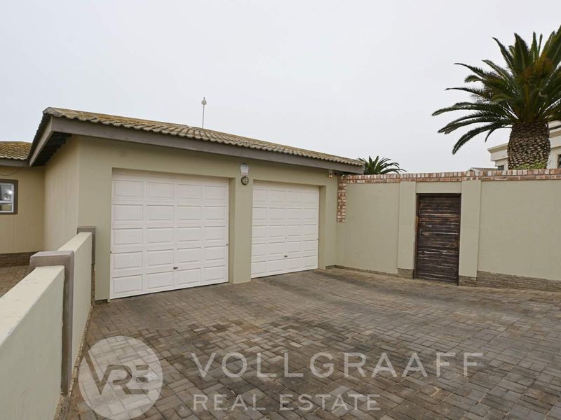 A double garage with white sectional doors, paved driveway, and secure boundary walling, providing convenient off-street parking.