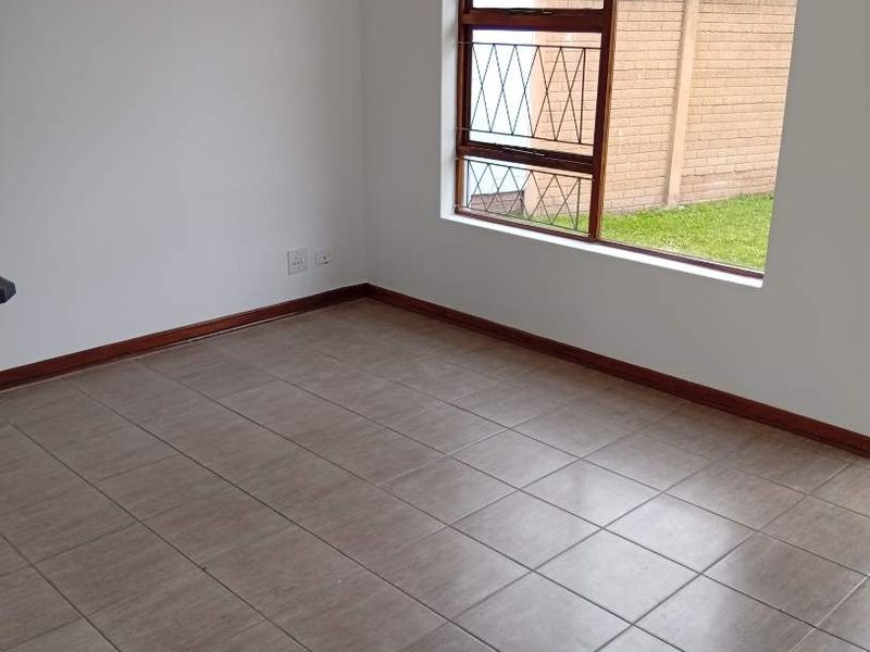 An empty bedroom featuring neutral tiled flooring, timber skirting boards, and a window fitted with security burglar bars.