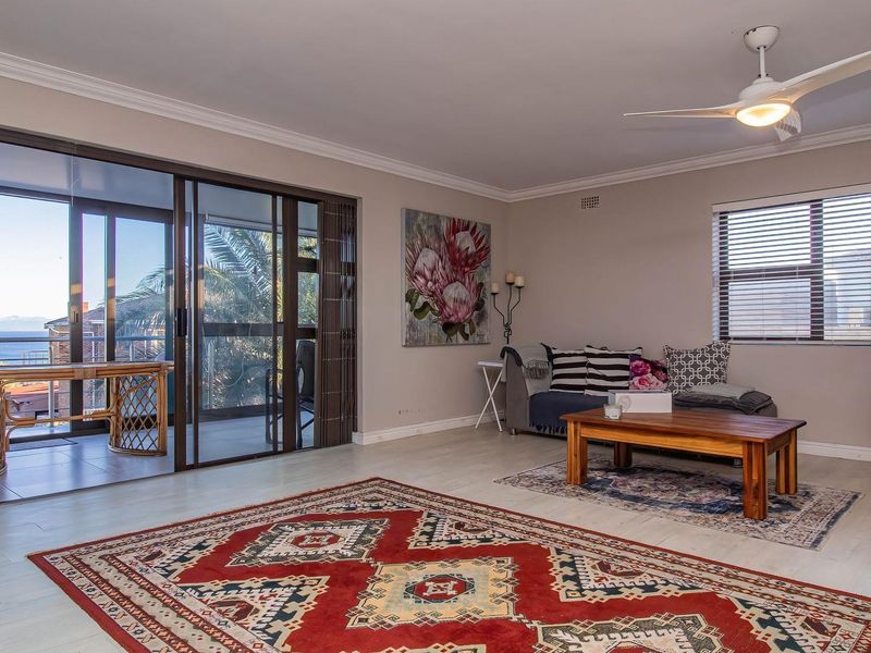 Spacious living room featuring light-toned flooring, a ceiling fan, and large sliding glass doors that open onto a balcony with scenic views.