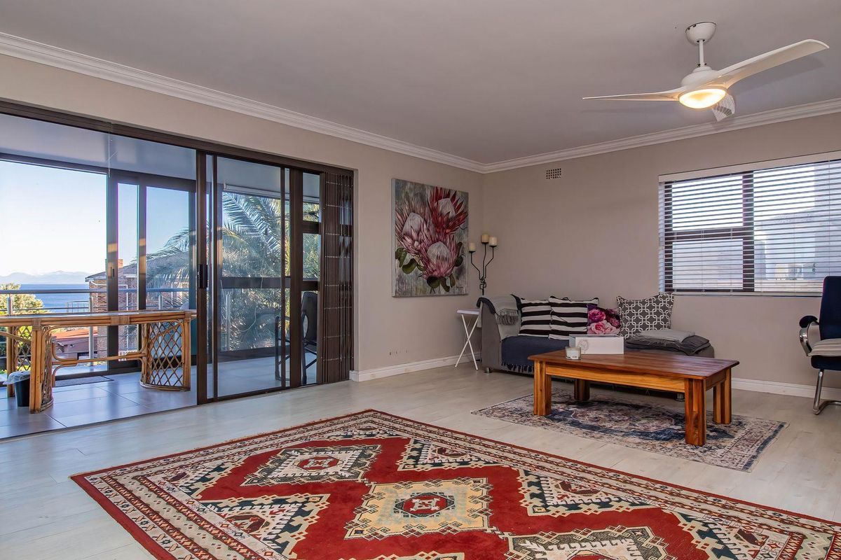 Spacious living room featuring light-toned flooring, a ceiling fan, and large sliding glass doors that open onto a balcony with scenic views.