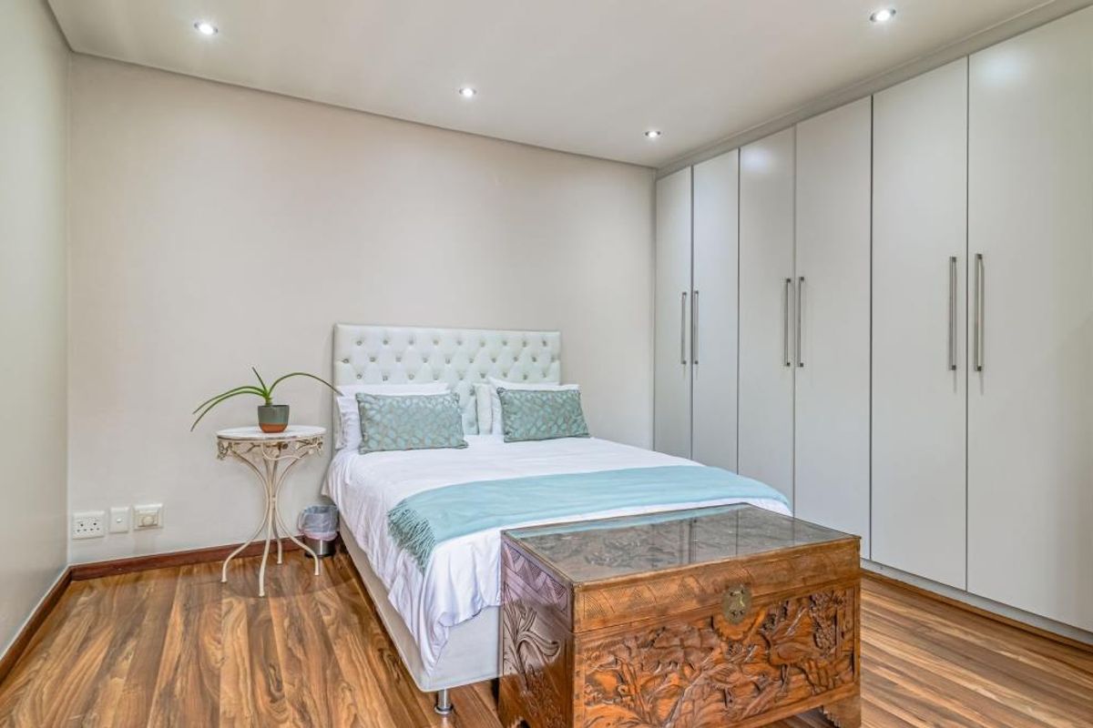 A well-maintained bedroom featuring modern laminate flooring, recessed downlighting, and extensive floor-to-ceiling built-in cupboards for ample storage.