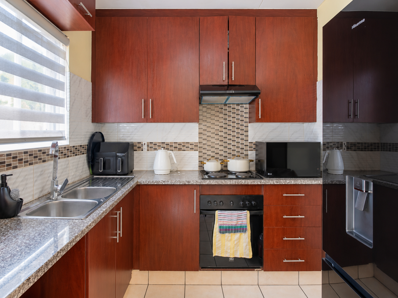 A functional kitchen featuring dark wood cabinetry, granite-look laminate countertops, a built-in oven with hob, and a stainless steel double sink.