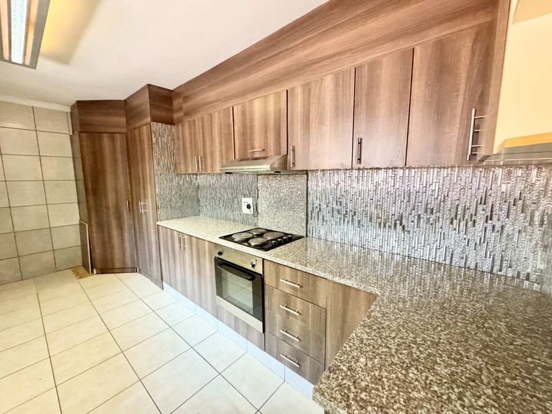 A modern kitchen featuring wood-finish cabinetry, granite countertops, a built-in electric oven and hob, and a decorative mosaic tile backsplash.
