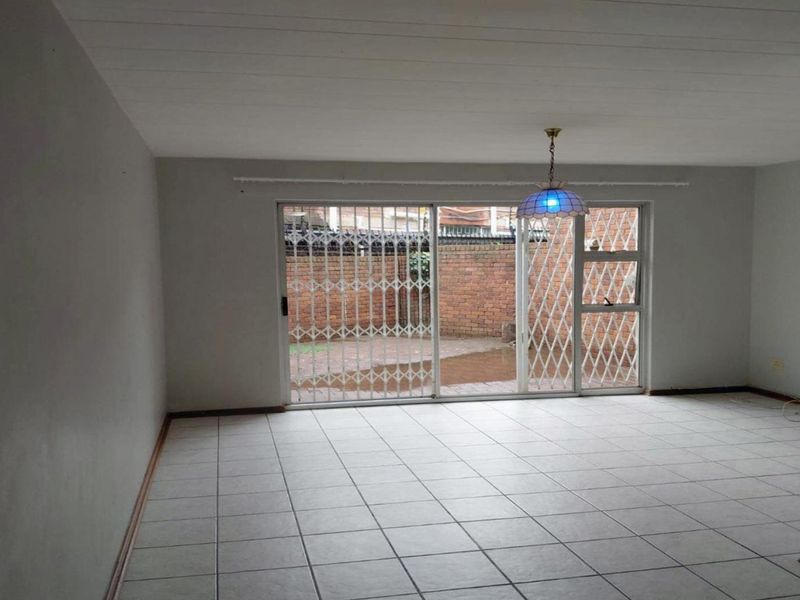 An empty living room featuring tiled flooring and a sliding glass door with a security gate, providing direct access to the rear patio area.